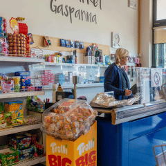Interior de tienda en Campeggio Gasparina, Véneto, Italia, con estantes de dulces y una cajera atendiendo.