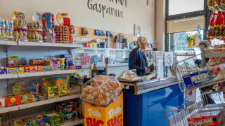 Interior de tienda en Campeggio Gasparina, Véneto, Italia, con estantes de dulces y una cajera atendiendo.