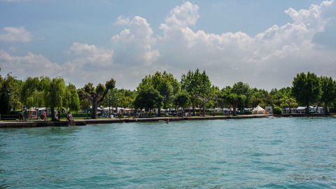 Vista al lago en Campeggio Gasparina, Véneto, Italia, con árboles, tiendas y campers junto a la orilla.
