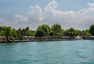 View of the lake at Campeggio Gasparina in Veneto, Italy, with lush trees, campers, and tents by the shore.