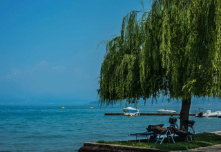 Entspannter Tag am See im Campeggio Gasparina, Venetien, Italien. Mann ruht im Schatten eines Baumes mit Booten im Hintergrund.