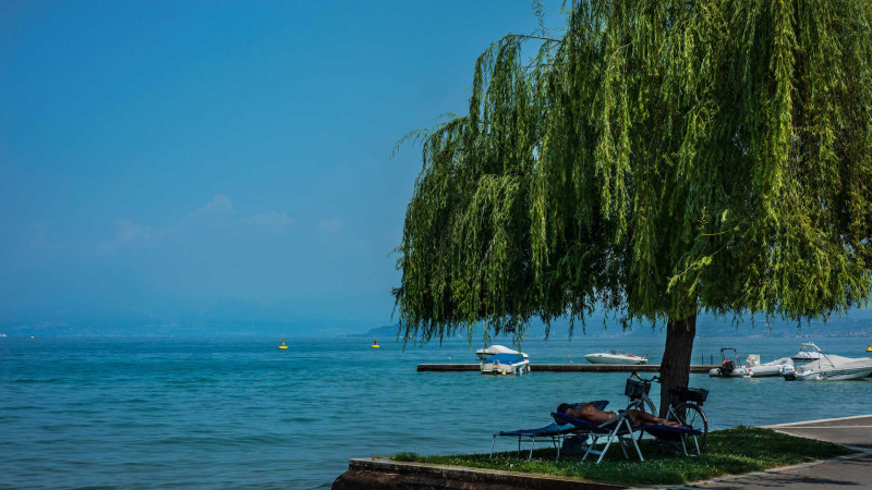 Relaxing day by the lake at Campeggio Gasparina, Veneto, Italy. Man rests under a tree with boats in the background.