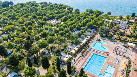 Vista aérea del parque vacacional Campeggio Gasparina en Véneto, Italia, con piscinas, cabañas y zonas arboladas junto al lago.
