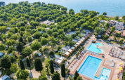 Aerial view of Campeggio Gasparina holiday park in Veneto, Italy, showing pools, cabins and lush greenery by a lake.