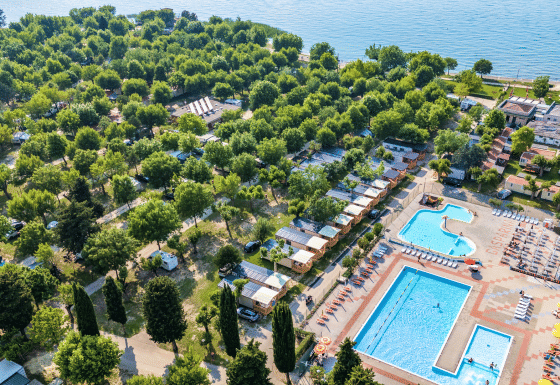 Aerial view of Campeggio Gasparina holiday park in Veneto, Italy, showing pools, cabins and lush greenery by a lake.