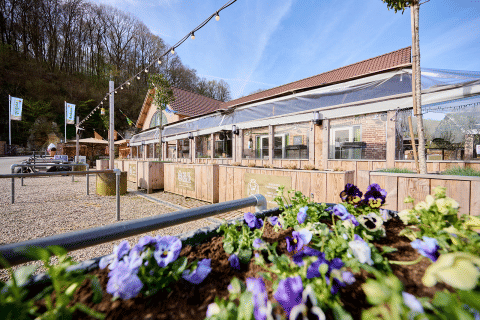 Flower bed and terrace at Camping 't Geuldal holiday park in Limburg, Netherlands, with trees and blue sky.