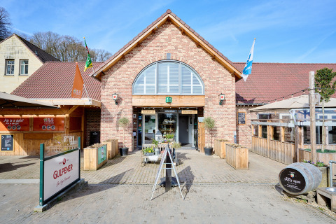 Entrada principal del Camping 't Geuldal en Limburg, Países Bajos, con terraza exterior y carteles visibles.
