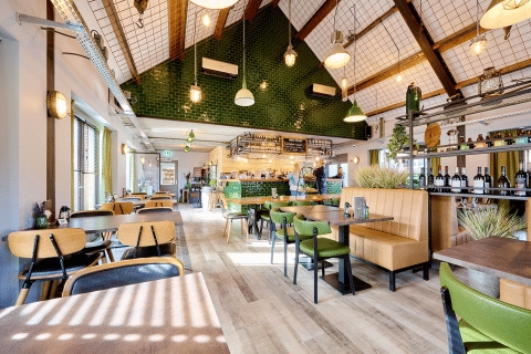 Interno di ristorante moderno e luminoso a Camping 't Geuldal, Limburgo, Paesi Bassi, con arredi verdi e in legno.