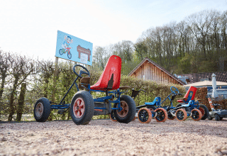 Børnepedalbiler linet op på grusvej ved Camping 't Geuldal i Limburg, Holland, med hække og skilte.