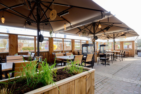 Zona exterior para comer en Camping 't Geuldal, Limburg, Países Bajos, con mesas de madera y sombrillas grandes
