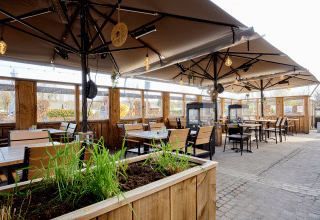 Zona exterior para comer en Camping 't Geuldal, Limburg, Países Bajos, con mesas de madera y sombrillas grandes