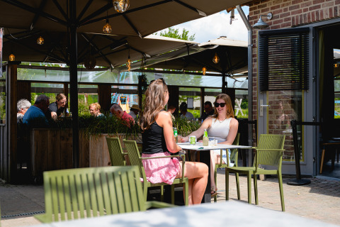 Dos mujeres bebiendo en una terraza soleada en Camping 't Geuldal, un parque vacacional en Limburg, Países Bajos.