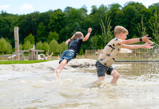 Twee jongens ravotten en spetteren in het water op een camping, omringd door bomen in Limburg, Nederland.