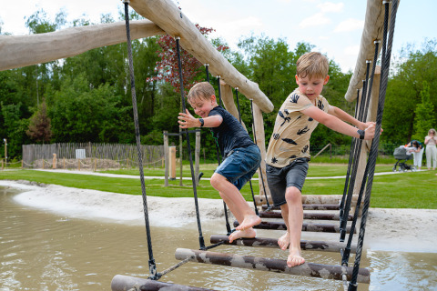 Dos niños juegan en un puente de cuerda sobre agua en Camping 't Geuldal en Limburg, Países Bajos.
