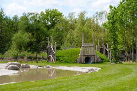 Area giochi con collina, scivolo a tunnel e stagno al Camping 't Geuldal, parco vacanze in Limburgo, Paesi Bassi.