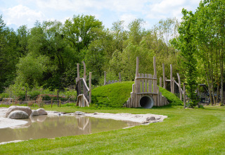 Speelheuvel met tunnel en vijver bij Camping 't Geuldal vakantiepark in Limburg, Nederland, op een zonnige dag.