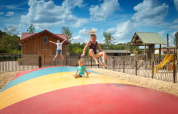 Børn leger og hopper på en stor farverig hoppepude ved Camping 't Geuldal, Limburg, Holland, med legeplads i baggrunden.