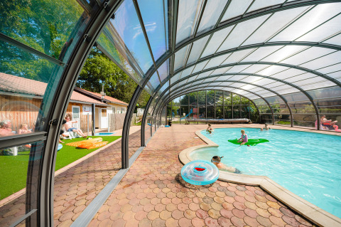 Piscina cubierta con familias nadando y relajándose en Camping Au Clos de La Chaume, Grand Est, Francia.