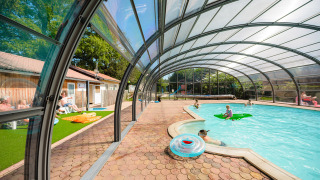 Piscina cubierta con familias nadando y relajándose en Camping Au Clos de La Chaume, Grand Est, Francia.