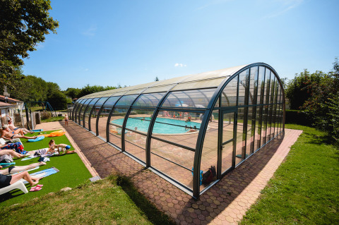 Piscina cubierta con huéspedes tomando el sol en Camping Au Clos de La Chaume, Grand Est, Francia.