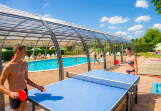 Twee jongeren spelen tafeltennis bij een overdekt zwembad op Camping Au Clos de La Chaume in Frankrijk.