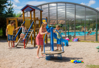 Famiglie si divertono nell’area giochi e in piscina al Camping Au Clos de La Chaume, Grand Est, Francia al sole.