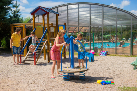 Familias disfrutan del parque infantil y la piscina en Camping Au Clos de La Chaume, Grand Est, Francia al sol.