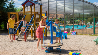 Familias disfrutan del parque infantil y la piscina en Camping Au Clos de La Chaume, Grand Est, Francia al sol.