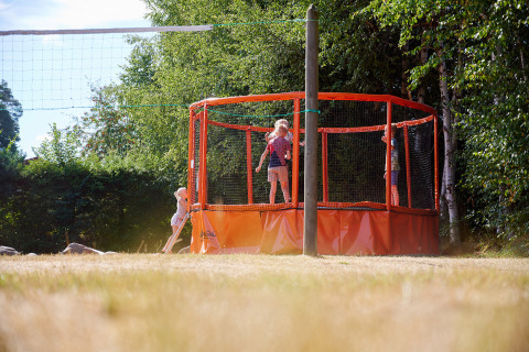 Niños juegan en una cama elástica junto a una cancha de voleibol en Camping Au Clos de La Chaume, Grand Est, Francia.