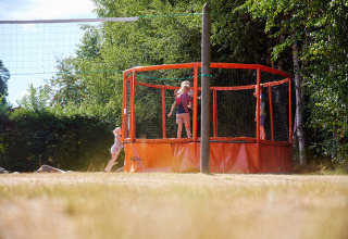 Kinder spielen auf einem Trampolin neben einem Volleyballfeld im Grünen bei Camping Au Clos de La Chaume, Grand Est.