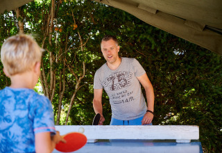 Un uomo e un bambino giocano a ping pong all'aperto sotto una tettoia in un campeggio nel Grand Est, Francia.