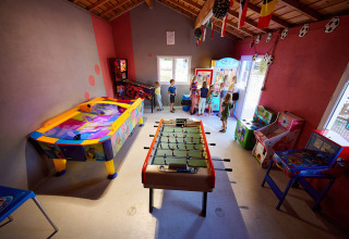Bambini che giocano in una sala giochi colorata con calcio balilla, air hockey e cabinati in un villaggio vacanze francese.