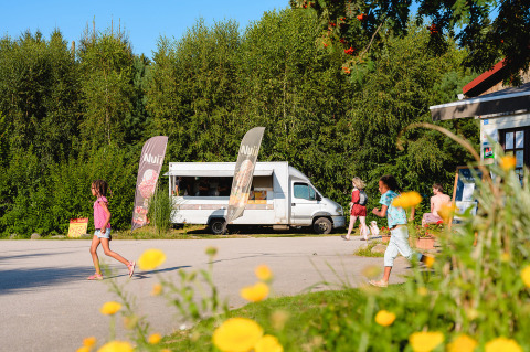 Bambini e adulti si godono il sole vicino a un food truck al Camping Au Clos de La Chaume, Grand Est, Francia.