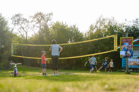 Niños y adultos juegan al fútbol junto a una red de voleibol en Camping Au Clos de La Chaume, Grand Est, Francia.