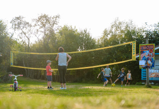 Kinderen en volwassenen spelen voetbal naast een volleybalnet op Camping Au Clos de La Chaume, Frankrijk.