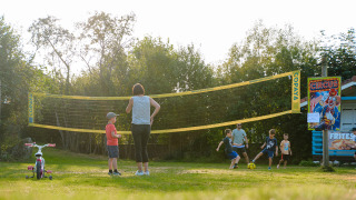 Niños y adultos juegan al fútbol junto a una red de voleibol en Camping Au Clos de La Chaume, Grand Est, Francia.