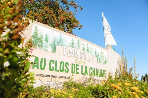 Cartel de entrada de Camping Au Clos de La Chaume en Grand Est, Francia, rodeado de vegetación y flores.