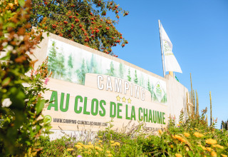 Indgangen til Camping Au Clos de La Chaume i Grand Est, Frankrig, med flag og frodige planter omkring.