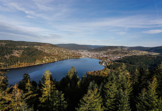 Udsigt over en sø omgivet af bakker og tæt skov ved Camping Au Clos de La Chaume i Grand Est, Frankrig.
