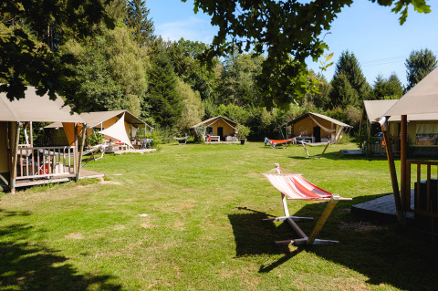 Tiendas y hamacas en Camping Au Clos de La Chaume, rodeado de naturaleza en Grand Est, Francia.