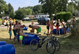 Gezinnen en kinderen maken vlotten met blauwe vaten op Camping Betuwe, een vakantiepark in Gelderland, Nederland.