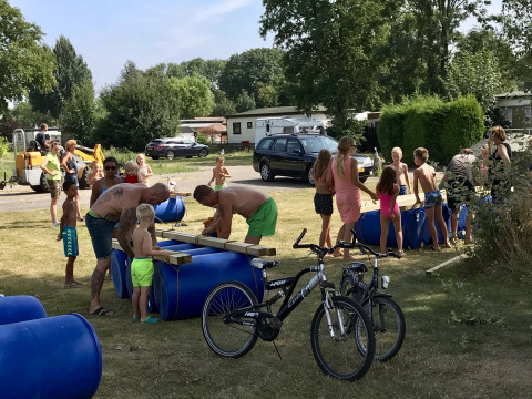 Familier og børn bygger tømmerflåder med blå tønder på Camping Betuwe, en ferielejr i Gelderland, Holland.