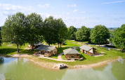 Luftfoto af Camping Betuwe, et feriested i Gelderland, Holland, med telte ved en sø og grønne træer.