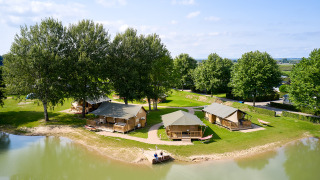 Luchtfoto van Camping Betuwe, een vakantiepark in Gelderland, Nederland, met tenten aan een klein meer.