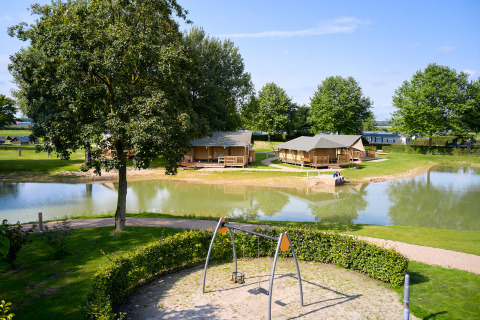 Tiendas glamping junto a un estanque y parque infantil en primer plano en Camping Betuwe, Gelderland, Países Bajos.