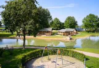 Glamping tenten aan een vijver met speelplein vooraan bij Camping Betuwe, Gelderland, Nederland, op zonnige dag.
