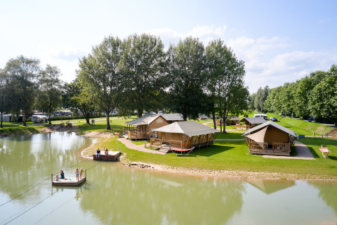Cabañas junto al lago y personas relajándose en Camping Betuwe, Gelderland, Países Bajos, en un día soleado.