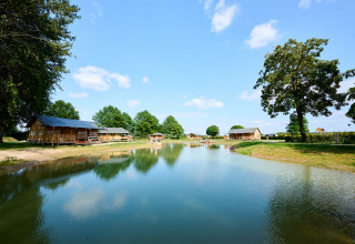 Parc de vacances Camping Betuwe à Gelderland, Pays-Bas, avec cabanes près d’un étang et ciel ensoleillé.
