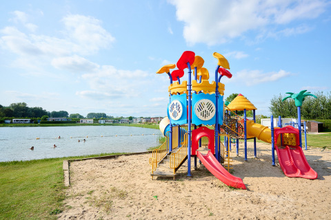 Parque infantil junto al lago en Camping Betuwe, Gelderland, Países Bajos, con toboganes coloridos y arena.