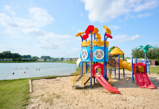 Speeltuin bij het meer op Camping Betuwe, Gelderland, Nederland, met kleurrijke glijbanen en zand.